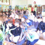 Dzieci i nauczyciele uważnie słuchają prelekcji o recyklingu podczas spotkania edukacyjnego w szkole.