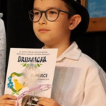 Chłopiec w stroju ludowym trzyma dyplom i nagrodę za zajęcie II miejsca w konkursie instrumentalistów podczas 42. Konkursu Muzyk, Śpiewaków Ludowych i Drużbów Weselnych "Druzbacka".