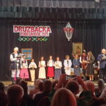 Uczestnicy konkursu "Druzbacka" w Podegrodziu 2025 stoją na scenie w strojach regionalnych, trzymając dyplomy i nagrody podczas oficjalnej ceremonii wręczenia nagród.