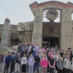 Grupa uczniów klas 1–3 stoi przed wejściem do Parku Dinozaurów w Zatorlandzie. W tle ogromna brama stylizowana na prehistoryczną skałę i figura dinozaura.