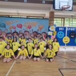 Uczennice prezentują występ taneczny na sali gimnastycznej. Dzieci w żółtych koszulkach poruszają się w zorganizowanym układzie choreograficznym.