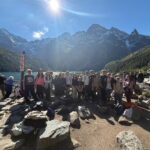 Grupa uczniów i opiekunów podczas wycieczki nad Morskie Oko. Uczestnicy pozują do wspólnego zdjęcia na tle jeziora i ośnieżonych tatrzańskich szczytów.