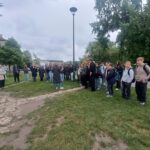 Na zdjęciu grupa uczniów z opiekunami oraz przewodnikiem. Stoją na ścieżce, w tle są drzewa.