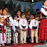 Grupa dzieci w góralskich strojach śpiewa na scenie podczas Gorczańskiego Spotkania z Janem Pawłem II w Lubomierzu-Rzekach. Chłopcy w białych koszulach i portkach stoją w pierwszym rzędzie.