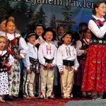 Grupa dzieci w góralskich strojach śpiewa na scenie podczas Gorczańskiego Spotkania z Janem Pawłem II w Lubomierzu-Rzekach. Chłopcy w białych koszulach i portkach stoją w pierwszym rzędzie.
