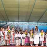 Grupa dzieci w strojach regionalnych i eleganckich ubraniach występuje na scenie podczas Gorczańskiego Spotkania z Janem Pawłem II w Lubomierzu-Rzekach.