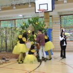 Szewczyk Dratewka pomaga pszczołom przy ulu w trakcie inscenizacji, obok kobieta w stroju kota czyta tekst.