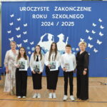 Czworo uczniów trzyma książki z lekturami, stojąc przed niebieskim tłem z napisem „Uroczyste zakończenie roku szkolnego 2024/2025”; obok nauczycielki.