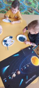 Dzieci tworzą planetę, malując papierowe talerzyki farbą w kolorze granatowym.
