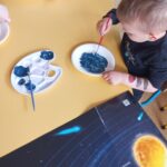 Dzieci tworzą planetę, malując papierowe talerzyki farbą w kolorze granatowym.