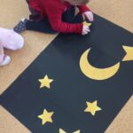 Dziewczynka nakleja żółte gwiazdy na czarnym kartonie.