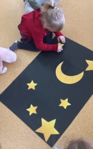 Dziewczynka nakleja żółte gwiazdy na czarnym kartonie.