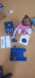 Dziewczynka siedzi na dywanie i przelicza granatowe przedmioty.