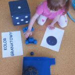 Dziewczynka siedzi na dywanie i przelicza granatowe przedmioty.