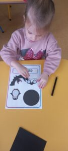 Dziewczynka siedzi przy stoliku i liczy czarne obrazki na karcie pracy.