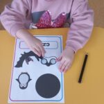 Dziewczynka siedzi przy stoliku i liczy czarne obrazki na karcie pracy.