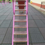 Schody o metalowej konstrukcji z antypoślizgowymi stopniami, prowadzące na podest zestawu zabawowego – stabilne, wyposażone w obustronne poręcze dla zwiększenia bezpieczeństwa dzieci.