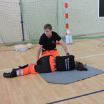 Ratownik demontruje na ratowniczce, jak należy ułożyć nogi poszkodowanego w pozycji bocznej ustalonej