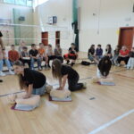 Trzy uczennice wykonują resucytację na fantomach pod czujnym okiem ratownika. Pozostali uczniowie obserwują przebieg resuscytacji