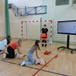 Trzy uczennice wykonują resucytację na fantomach pod czujnym okiem ratownika. Pozostali uczniowie obserwują przebieg resuscytacji