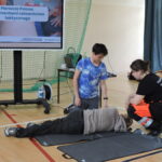 Uczeń układa drugiego ucznia w pozycji bocznej pod czujnym okiem ratowniczki