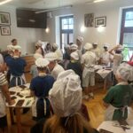 Uczniowie ubrani w czarpki i fartuchy ochronne słuchają wykładu o rodzajach czekolady