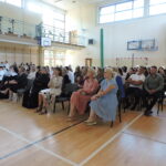 „Rodzice, uczniowie i zaproszeni goście siedzący w sali gimnastycznej podczas akademii rozpoczęcia roku.”