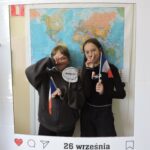 Dwie dziewczyny pozują do zdjęcia w dekoracyjnej ramce z napisem Europejski Dzień Języków i datą 26 września. Obie trzymają w rękach francuskie flagi i napisy. W tle widoczna jest mapa świata.
