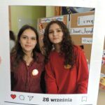 Dwie dziewczyny pozują do zdjęcia w dekoracyjnej ramce z napisem Europejski Dzień Języków i datą 26 września. W tle widoczna jest dekoracja związana z dniem języków.