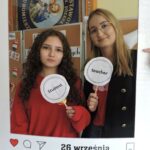 Dziewczyna i nauczycielka pozują do zdjęcia w dekoracyjnej ramce z napisem Europejski Dzień Języków i datą 26 września. W tle widoczna jest dekoracja związana z dniem języków i sztandar.