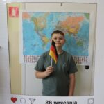 Jeden chłopiec pozuje do zdjęcia w dekoracyjnej ramce z napisem Europejski Dzień Języków i datą 26 września.. Trzyma w ręce niemiecką flagę. W tle widoczna jest mapa świata.