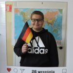 Jeden chłopiec pozuje do zdjęcia w dekoracyjnej ramce z napisem Europejski Dzień Języków i datą 26 września. Trzyma w ręce niemiecką flagę. W tle widoczna jest mapa świata.