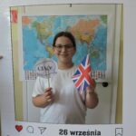 Jedna dziewczyna pozuje do zdjęcia w dekoracyjnej ramce z napisem Europejski Dzień Języków i datą 26 września. Trzyma w ręce brytyjską flagę i napis Ciao. W tle widoczna jest mapa świata.