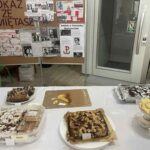 Stół przykryty białym obrusem z wystawionymi ciastami i słodkościami przygotowanymi przez uczniów i rodziców na kiermasz charytatywny w ramach akcji BohaterON. W tle tablice z plakatami i informacjami o Powstaniu Warszawskim.