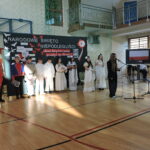 Uczniowie w strojach historycznych stoją na tle dekoracji „Narodowe Święto Niepodległości” podczas szkolnej akademii.