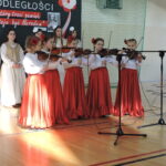 Grupa dziewczynek gra na skrzypcach przed dekoracją Święta Niepodległości