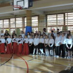 Duża grupa uczniów, młodszych i starszych, stoi razem podczas zakończenia akademii.