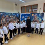 Pierwszoklasiści stoją w rzędzie podczas uroczystego pasowania, wysłuchując słów nauczyciela