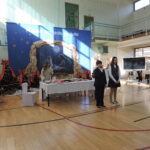 Uczniowie prezentują fragment szkolnego spotkania świątecznego na sali gimnastycznej, przy stole wigilijnym.