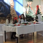 Uczennice siedzą przy stole wigilijnym podczas szkolnego spotkania bożonarodzeniowego; w tle świąteczna dekoracja.