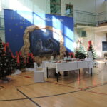 Scena szkolnego spotkania bożonarodzeniowego z dekoracją, szopką oraz stołem wigilijnym.