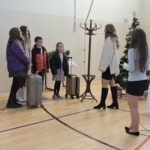 Uczniowie biorą udział w inscenizacji podczas szkolnego spotkania świątecznego; stoją obok dekoracji.