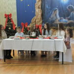 Uczniowie siedzą przy stole wigilijnym podczas szkolnej uroczystości bożonarodzeniowej.