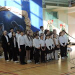 Chór uczniowski występuje na scenie podczas szkolnej uroczystości bożonarodzeniowej.