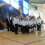 Chór uczniów śpiewa na tle dekoracji bożonarodzeniowej z szopką.