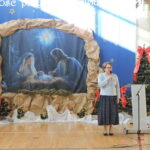 Dyrektorka przemawia do mikrofonu na tle dekoracji bożonarodzeniowej.