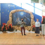 Wójt przemawia do mikrofonu na tle dekoracji bożonarodzeniowej.