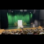 Scena V Gali Wolontariatu 2025 z dekoracją świetlną w kolorze zielonym; prowadzący i zaproszeni goście stoją na scenie.