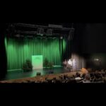 Scena V Gali Wolontariatu 2025 z dekoracją świetlną w kolorze zielonym; prowadzący i zaproszeni goście stoją na scenie.