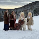 Grupa dzieci z zespołu „Śwarni Lubomiyrzanie” stoi na tle ośnieżonego lasu. Dwoje dzieci trzyma instrumenty smyczkowe, pozostali ubrani są w ciepłe, ludowe stroje. Scena przedstawia moment realizacji zdjęć plenerowych do teledysku kolędowego.